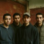 Vier jonge mannen met migratieachtergrond kijken serieus naar de camera