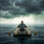 Persoon in een kleine rubberboot op open zee, roeiend onder donkere wolken richting een lichte horizon.