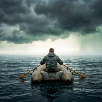 Persoon in een kleine rubberboot op open zee, roeiend onder donkere wolken richting een lichte horizon.