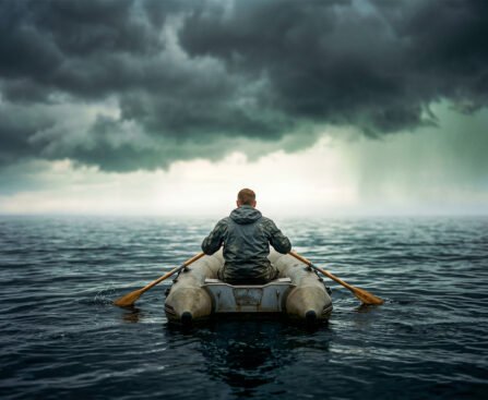 Persoon in een kleine rubberboot op open zee, roeiend onder donkere wolken richting een lichte horizon.