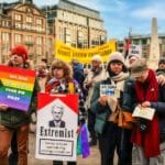 Protest op de Dam in Amsterdam tegen fascisme en haat, met demonstranten die borden vasthouden met teksten als “Wij zijn geen schild voor uw haat” en “Wij geloven in liefde”