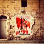 Vintage muur in Israël met een socialistische poster uit de jaren ’60. De poster toont arbeiders met een geweer en hamer, symbolen van arbeidersstrijd.