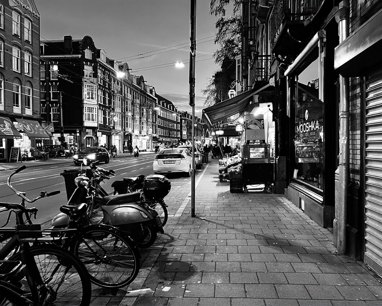 Zwart-wit foto van een rustige straat in Amsterdam, waar veel minderheden wonen, met winkels, fietsen en een stadse sfeer.