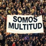 Een menigte activisten met een groot wit spandoek waarop de woorden ‘Somos multitud’ in het zwart staan. De scene straalt solidariteit en collectiviteit uit.