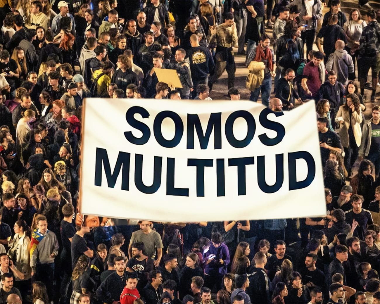 Een menigte activisten met een groot wit spandoek waarop de woorden ‘Somos multitud’ in het zwart staan. De scene straalt solidariteit en collectiviteit uit.