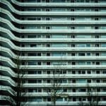 Galerijflat in Amsterdam-West met symmetrische balkons en zicht op kale bomen in de voorgrond.