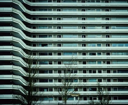 Galerijflat in Amsterdam-West met symmetrische balkons en zicht op kale bomen in de voorgrond.