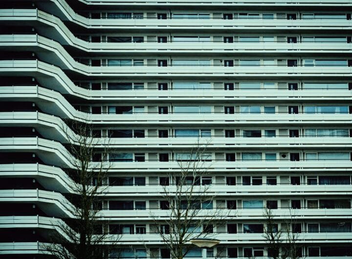 Galerijflat in Amsterdam-West met symmetrische balkons en zicht op kale bomen in de voorgrond.