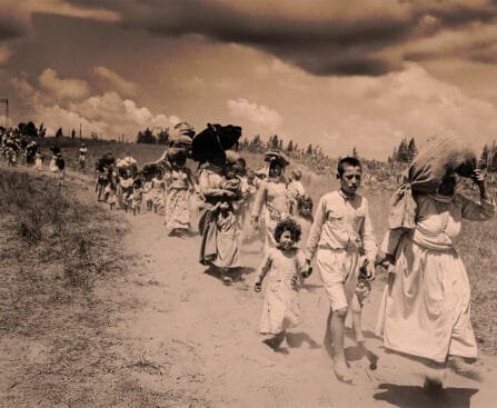 Palestijnse vluchtelingen lopen over een stoffige weg tijdens de Nakba in 1948, met bezittingen op hun rug en kinderen aan de hand.