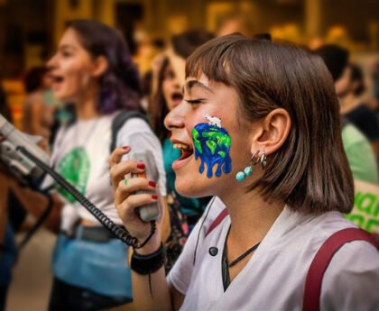 Jonge activist met een geschilderde smeltende aarde op haar gezicht, roepend in een megafoon tijdens een klimaatprotest.