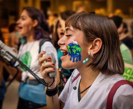 Jonge activist met een geschilderde smeltende aarde op haar gezicht, roepend in een megafoon tijdens een klimaatprotest.