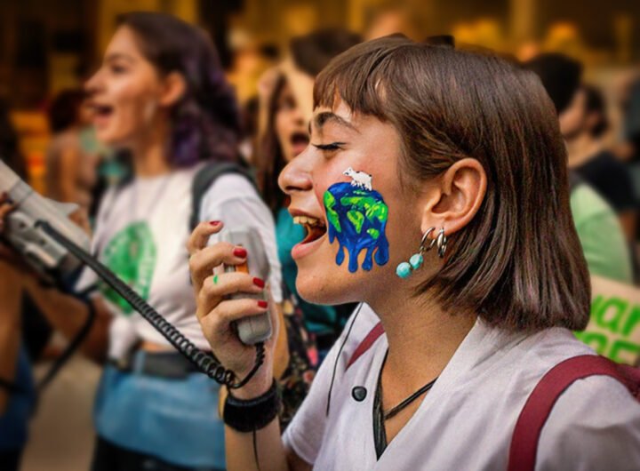 Jonge activist met een geschilderde smeltende aarde op haar gezicht, roepend in een megafoon tijdens een klimaatprotest.