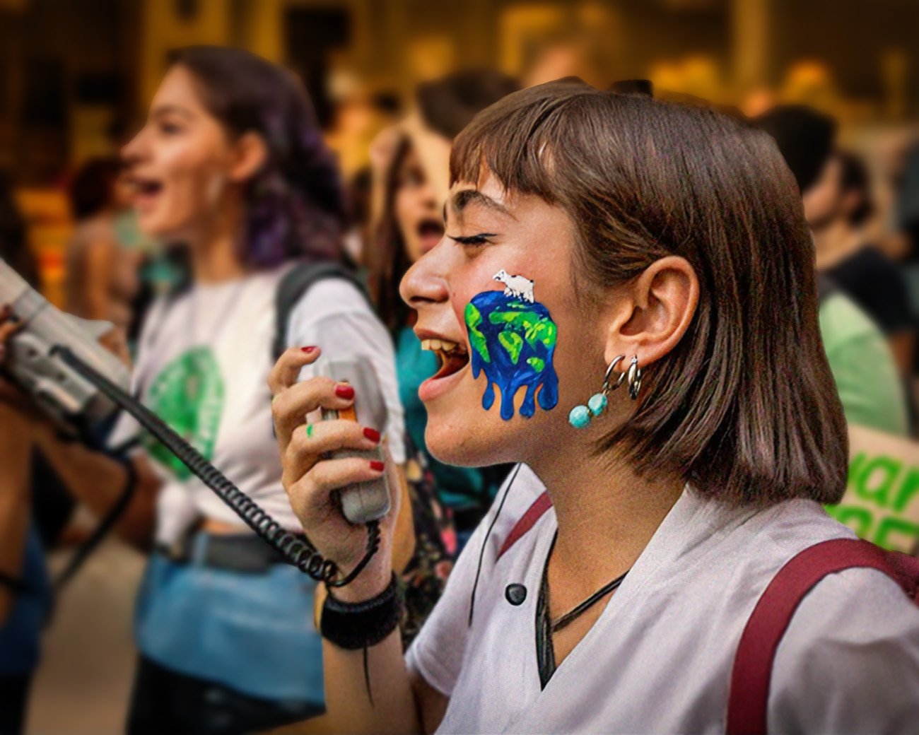 Jonge activist met een geschilderde smeltende aarde op haar gezicht, roepend in een megafoon tijdens een klimaatprotest.