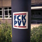 Sticker met de tekst “FCK PVV” op een lantaarnpaal, met op de achtergrond een gebouw en groenstrook.