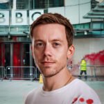 Journalist Owen Jones voor het BBC-gebouw, waar een schoonmaker rode verf verwijdert, symbool voor protest tegen de verslaggeving over Gaza.