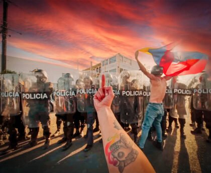 Een demonstrant met een vlag confronteert een rij oproerpolitie terwijl een hand met een middelvinger op de voorgrond zichtbaar is, tegen de achtergrond van een dramatische lucht.