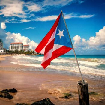 De vlag van Puerto Rico wappert op een strand met hotels en de oceaan op de achtergrond.