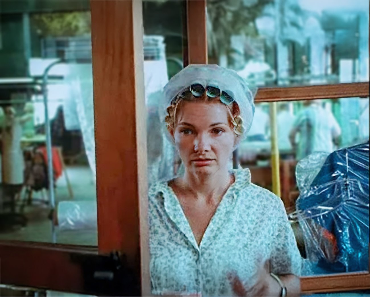 Still uit de film Wanda (1970) van Barbara Loden – een vrouw met krulspelden en netje staat voor een glazen deur in een industriële setting.