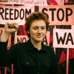 Daria Kozyreva heft haar vuist tijdens een vreedzaam protest tegen oorlog en voor vrijheid, omringd door borden met teksten als 'Stop War' en 'Freedom'.