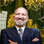 Howard Lutnik glimlacht zelfverzekerd voor een achtergrond vol geld en goudstaven