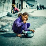 Jong meisje eet van de grond naast een lege pan in Gaza tijdens humanitaire crisis