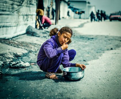 Jong meisje eet van de grond naast een lege pan in Gaza tijdens humanitaire crisis