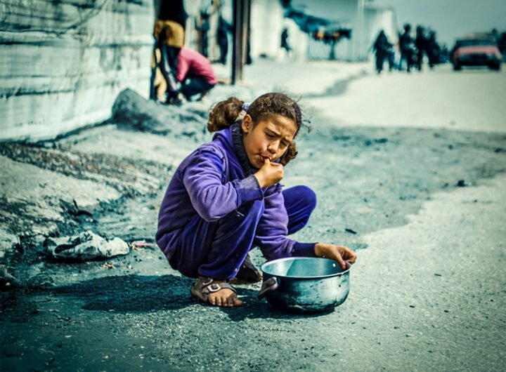 Jong meisje eet van de grond naast een lege pan in Gaza tijdens humanitaire crisis