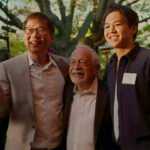 Robert Reich poseert met twee aanwezigen tijdens een bijeenkomst in de buitenlucht