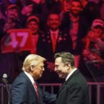 Trump en Musk schudden elkaar de hand tijdens een campagnebijeenkomst, omringd door juichende aanhangers met een bord met nummer 47.