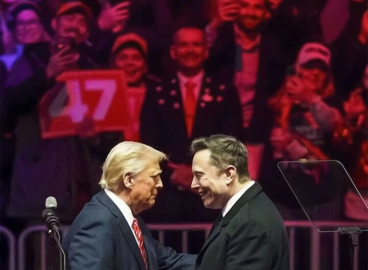 Trump en Musk schudden elkaar de hand tijdens een campagnebijeenkomst, omringd door juichende aanhangers met een bord met nummer 47.