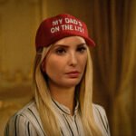 Vrouw met rood petje waarop staat “My dad’s on the list”, zittend in een klassieke kamer