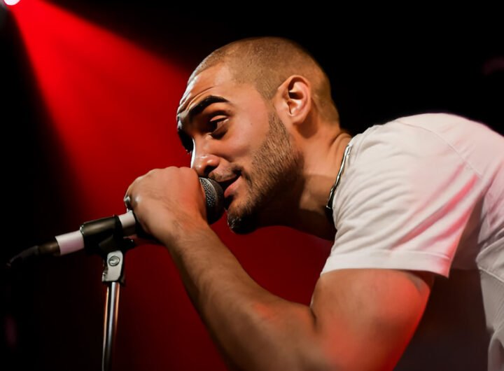 Lowkey rapt in de microfoon tijdens een optreden met rood podiumlicht