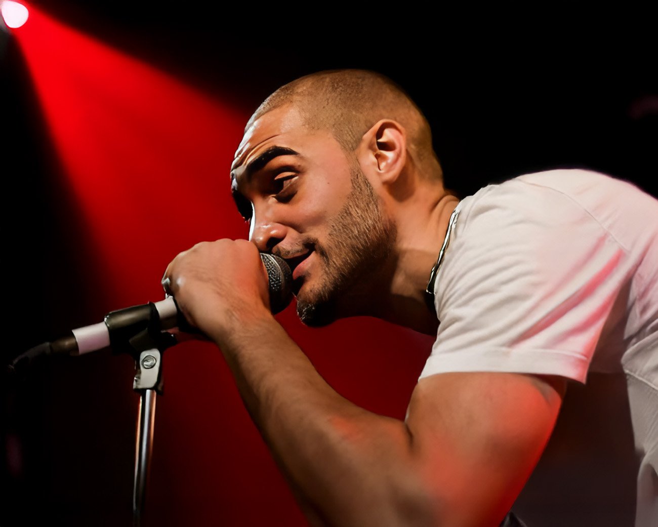 Lowkey rapt in de microfoon tijdens een optreden met rood podiumlicht