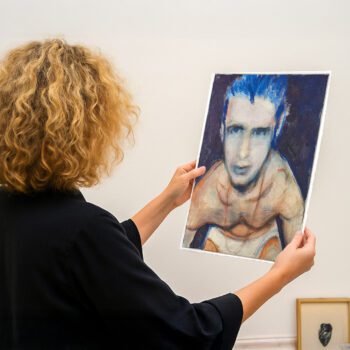 Persoon bekijkt een portret van een halfnaakte, kwetsbare man met blauwe haren in een kunstgalerie.