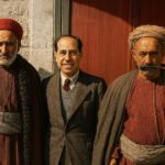 Twee traditioneel geklede Palestijnse mannen naast een Joodse man in westerse kleding, poserend voor een gebouw tijdens het Mandaat Palestina