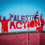 Twee activisten van Palestine Action houden een spandoek omhoog op een dak tijdens een protestactie