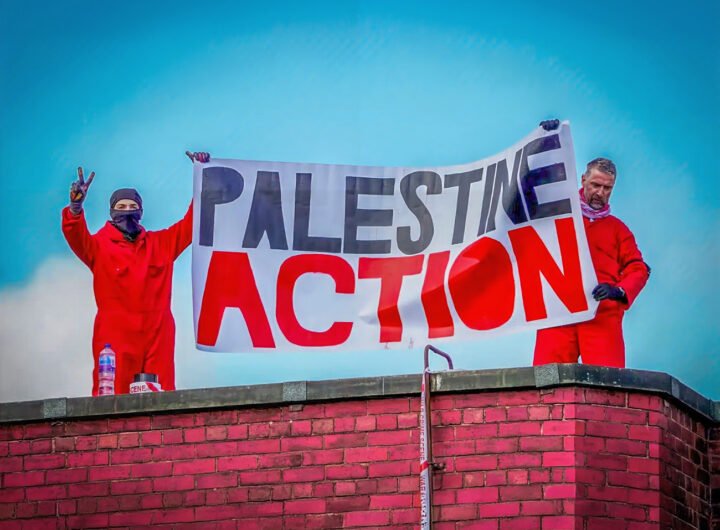 Twee activisten van Palestine Action houden een spandoek omhoog op een dak tijdens een protestactie