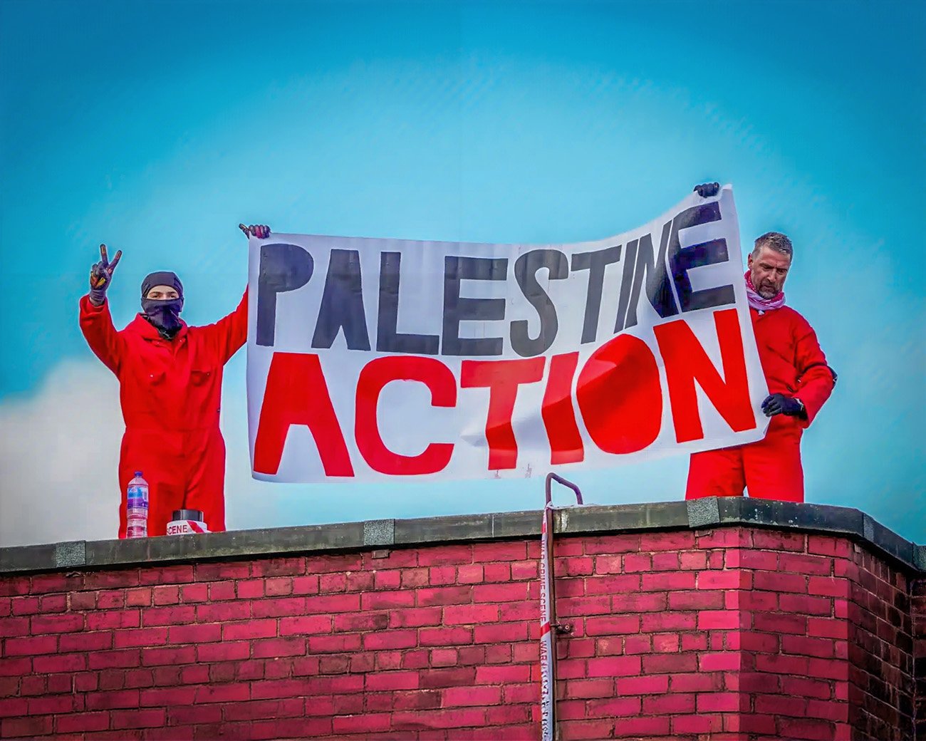 Twee activisten van Palestine Action houden een spandoek omhoog op een dak tijdens een protestactie