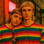 Twee jongeren in regenboogshirts leunen tegen elkaar als teken van verbondenheid en solidariteit
