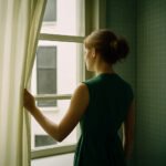 Vrouw kijkt stil uit het raam in een kamer met groene tegels