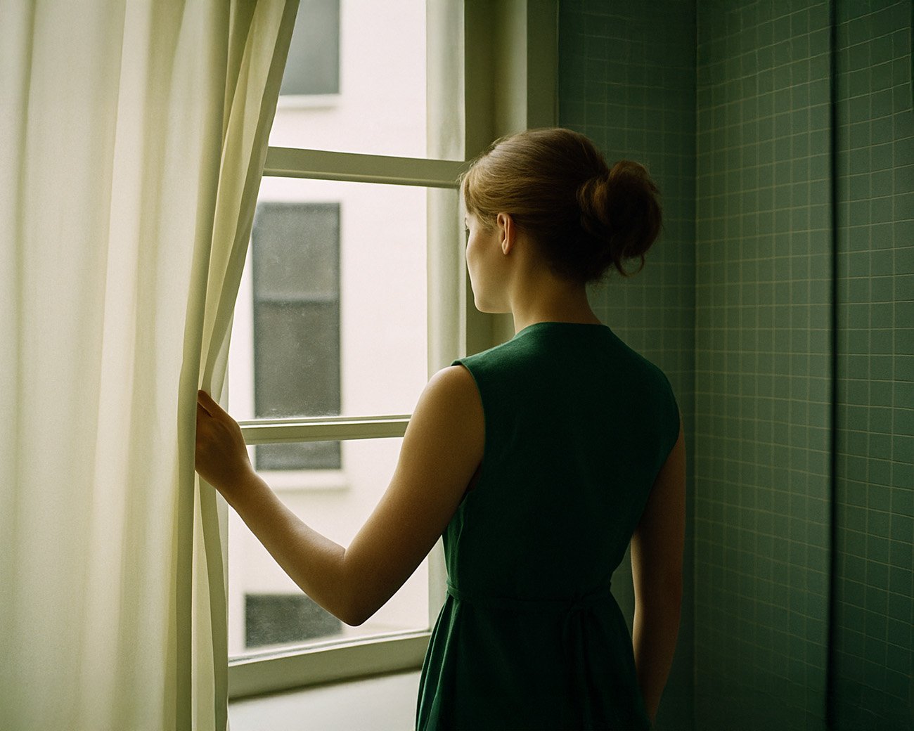 Vrouw kijkt stil uit het raam in een kamer met groene tegels
