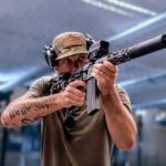 Pete Hegseth richt een semi-automatisch geweer terwijl zijn “We the People”-tatoeage zichtbaar is op zijn onderarm.