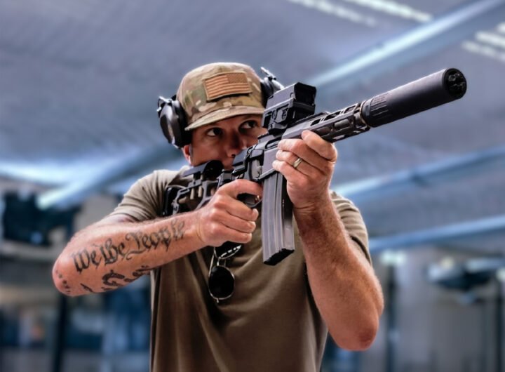 Pete Hegseth richt een semi-automatisch geweer terwijl zijn “We the People”-tatoeage zichtbaar is op zijn onderarm.