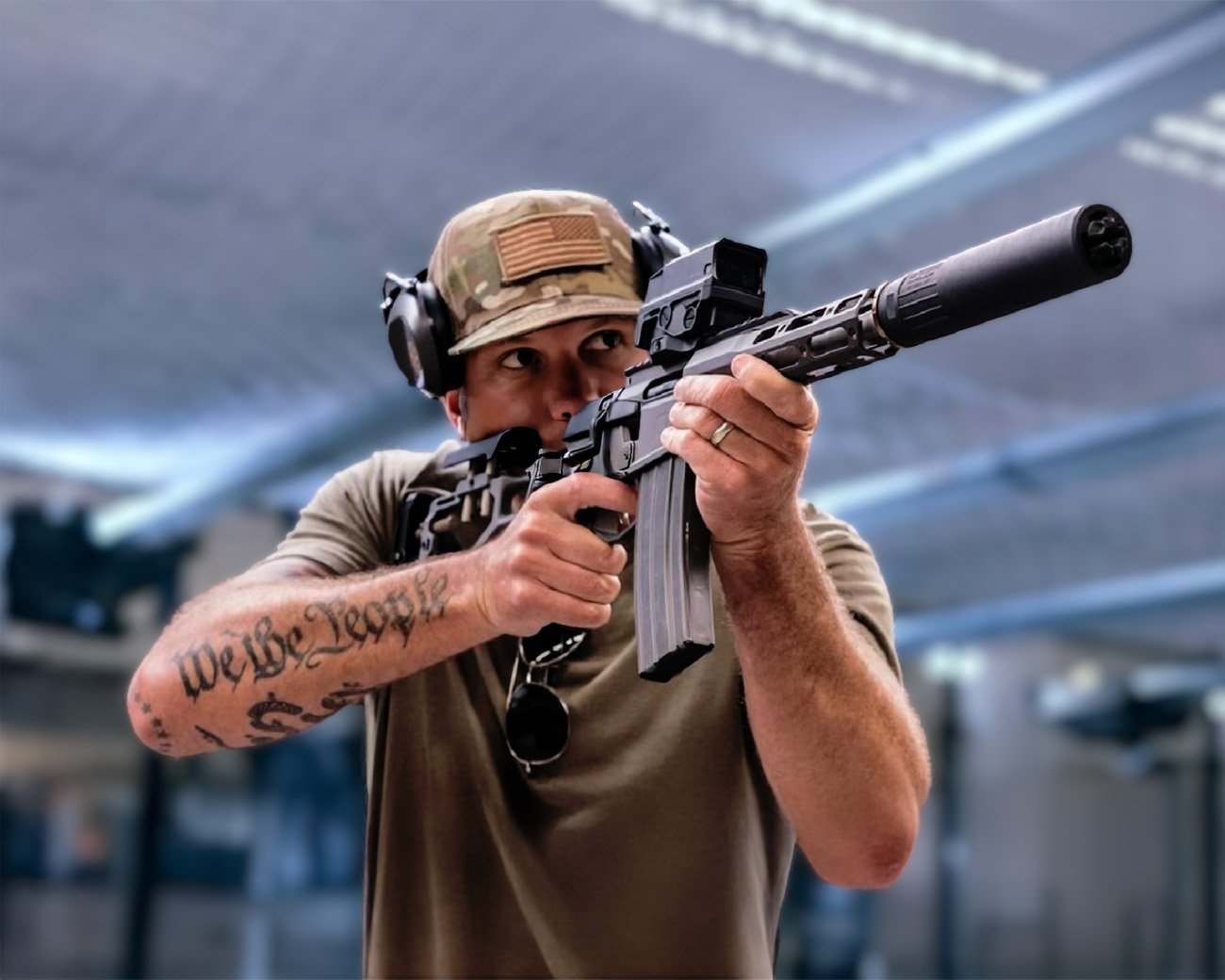Pete Hegseth richt een semi-automatisch geweer terwijl zijn “We the People”-tatoeage zichtbaar is op zijn onderarm.
