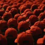 Grote groep mensen met identieke rode petjes, gezien van achteren