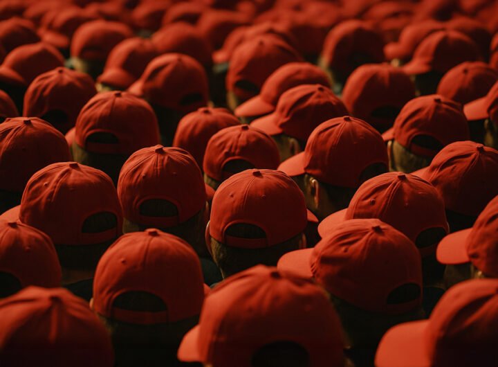 Grote groep mensen met identieke rode petjes, gezien van achteren