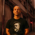 Man draagt een zwart T-shirt met portret van Rudolf Rocker in een stadsstraat.