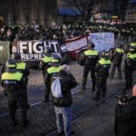 Politieagenten in gele hesjes houden een groep demonstranten met spandoeken tegen tijdens een protest tegen repressie en politiegeweld.