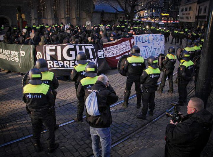 Politieagenten in gele hesjes houden een groep demonstranten met spandoeken tegen tijdens een protest tegen repressie en politiegeweld.
