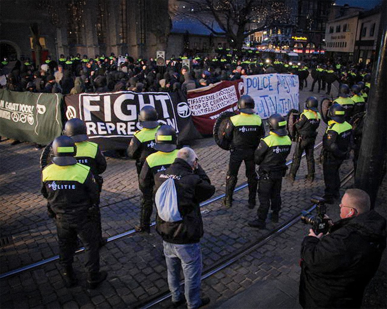 Politieagenten in gele hesjes houden een groep demonstranten met spandoeken tegen tijdens een protest tegen repressie en politiegeweld.